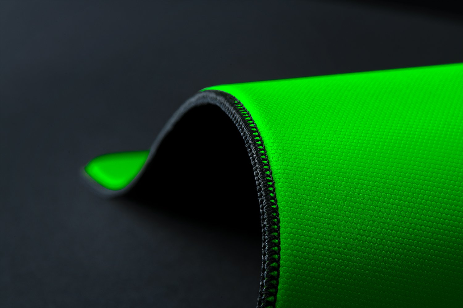 Una tela verde brillante con textura hexagonal se curva sobre una superficie negra.