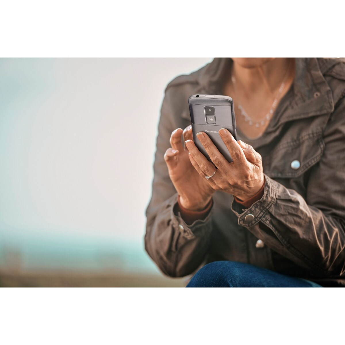 Una mujer sostiene un teléfono Panasonic gris en sus manos.