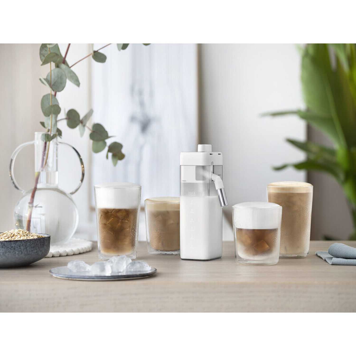 Iced coffee drinks with milk frother and ingredients on a wooden table.