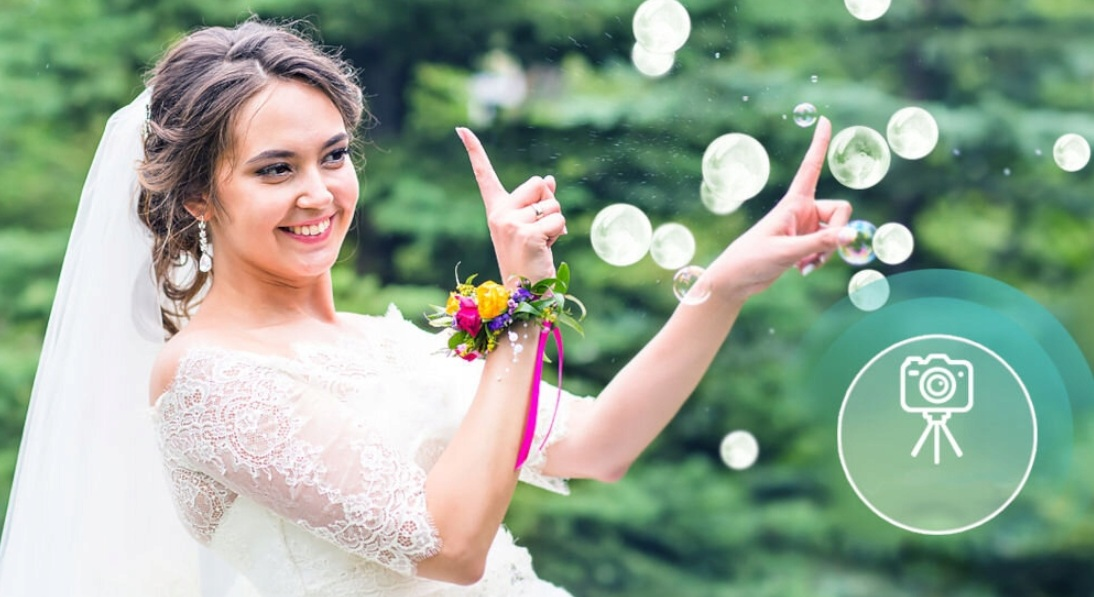 Panna młoda w welonie i z kwiatową bransoletką puszcza bańki mydlane na zewnątrz.
