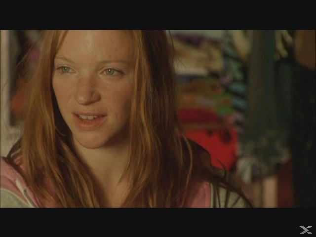 Eine junge Frau mit roten Haaren und Sommersprossen schaut nach links.