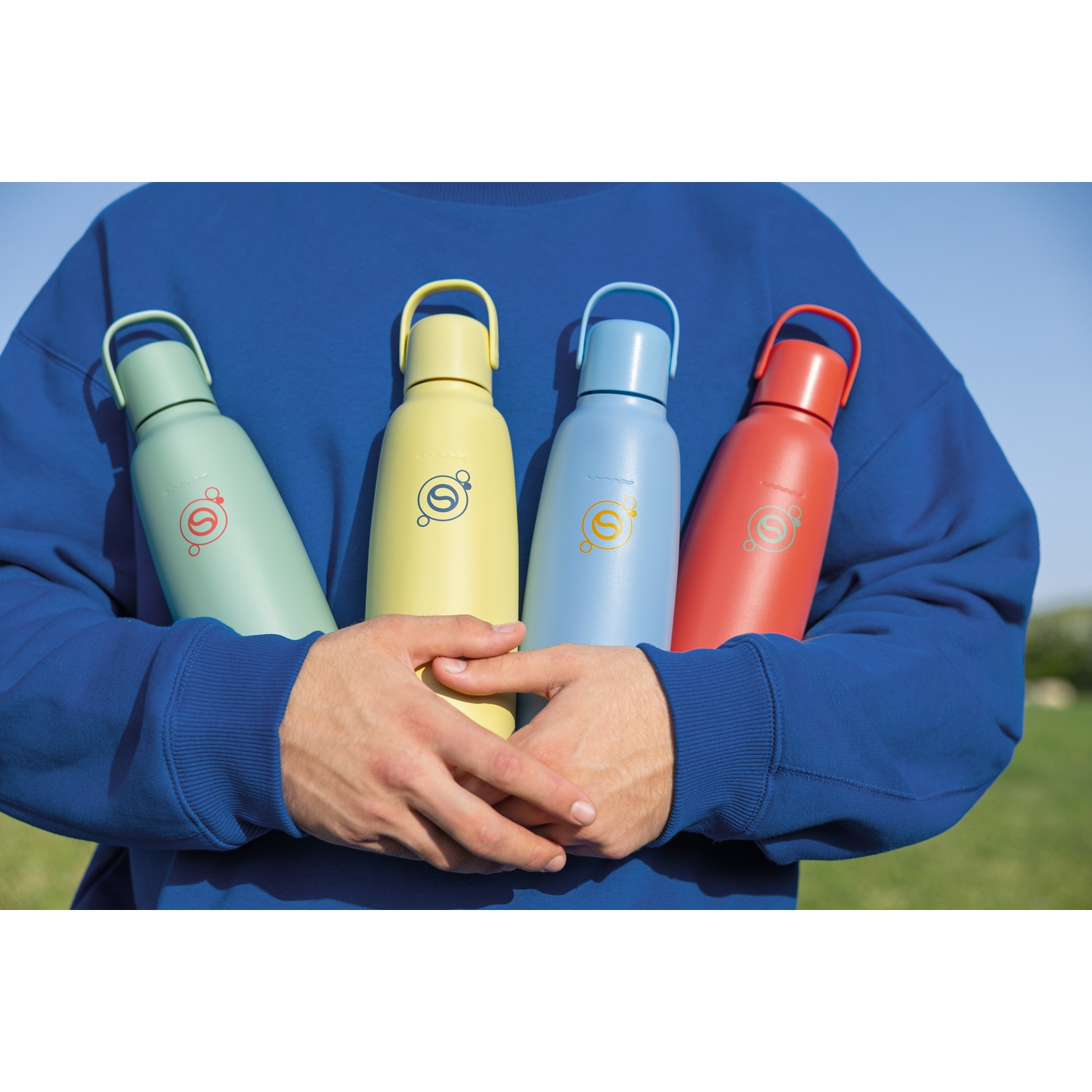 Une personne en sweat bleu tient quatre gourdes colorées.