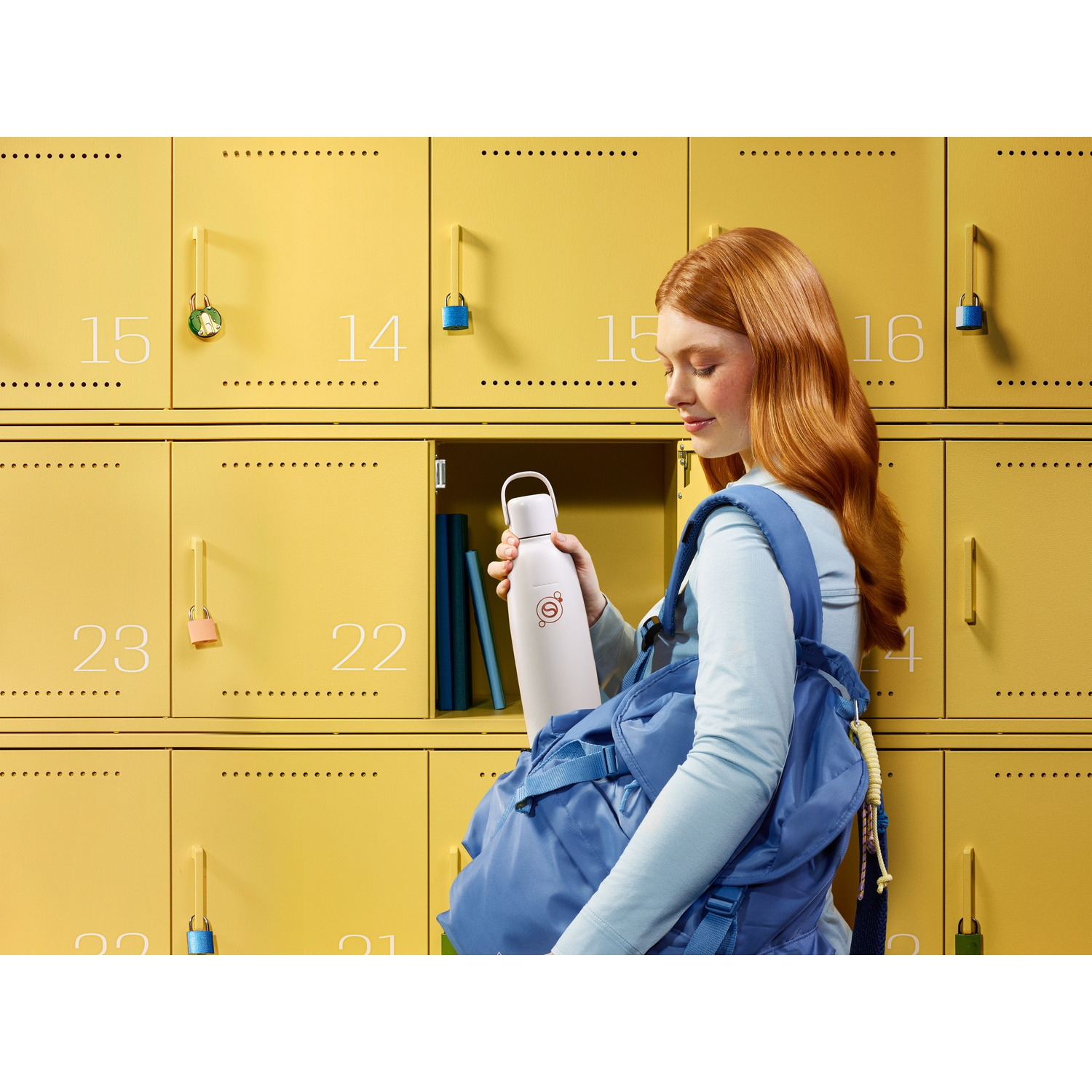 A red-haired girl retrieves a white bottle from a yellow locker.