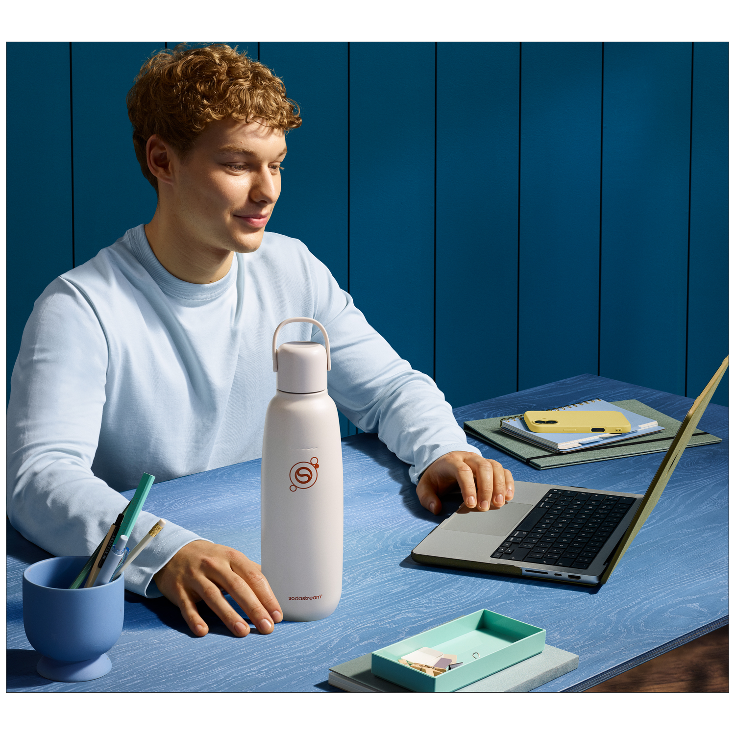 Man at desk with laptop and SodaStream bottle.