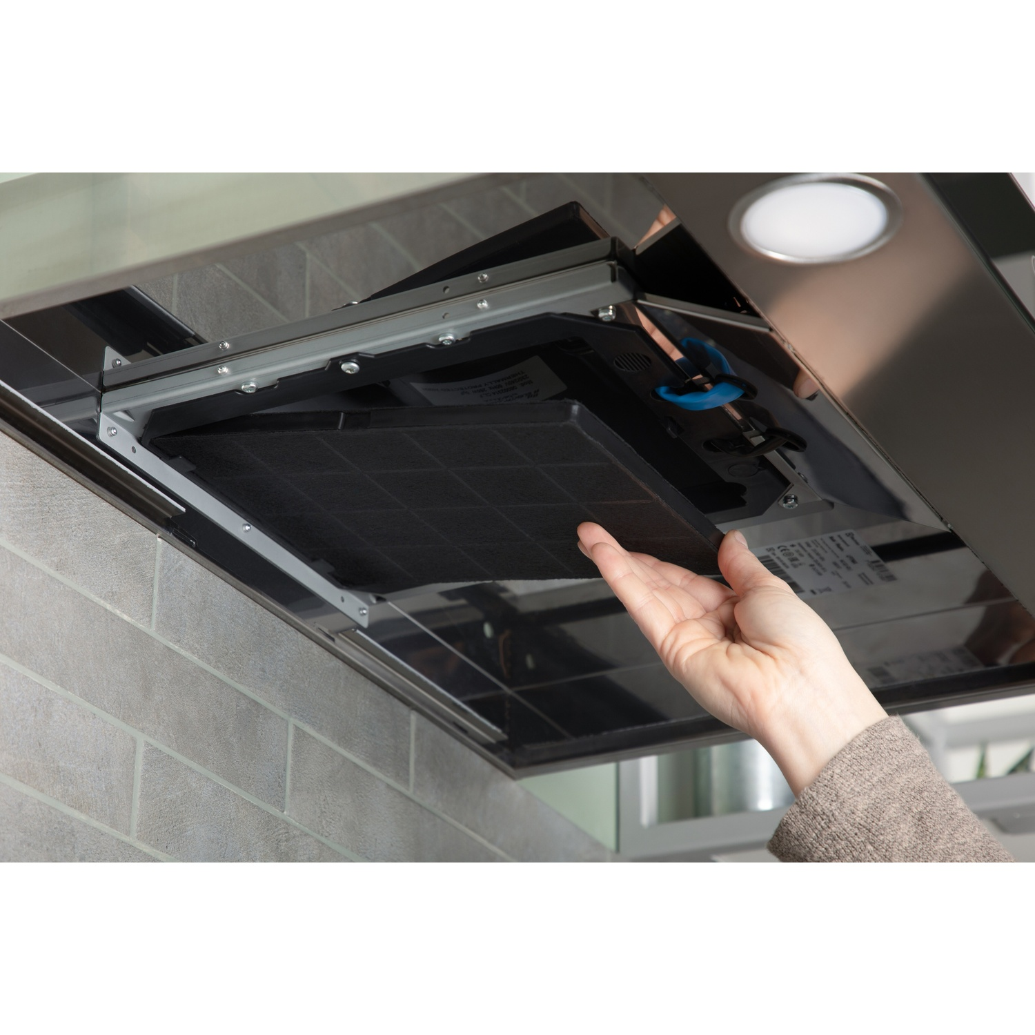 Hand installs a black charcoal filter into a range hood.