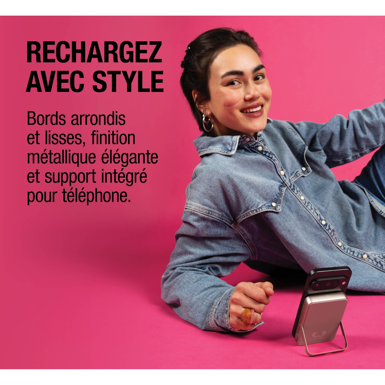 Une femme en chemise en jean est allongée sur un fond rose à côté d'un chargeur de téléphone.