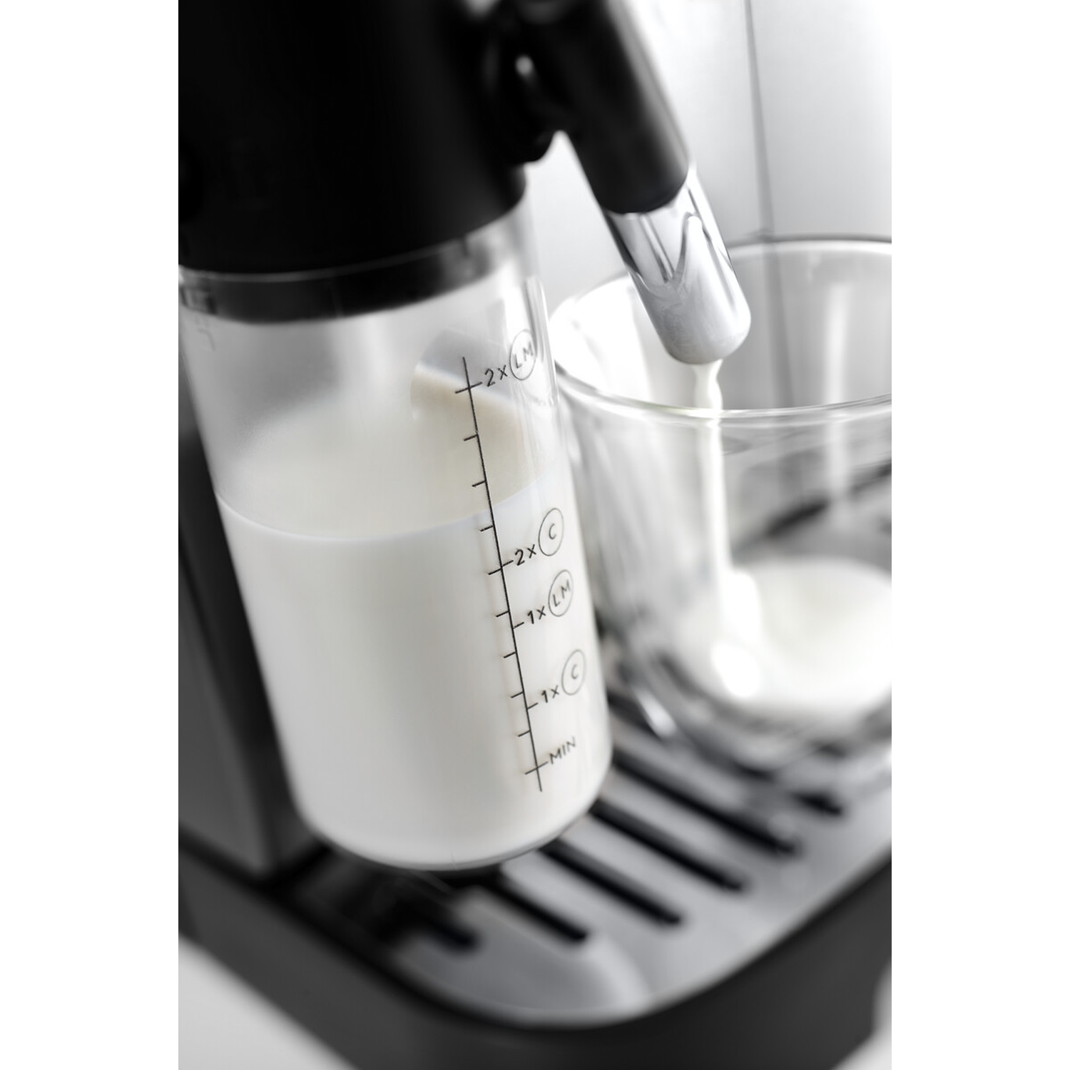 Een koffiezetapparaat stoomt melk in een helder glas naast een melkcontainer.