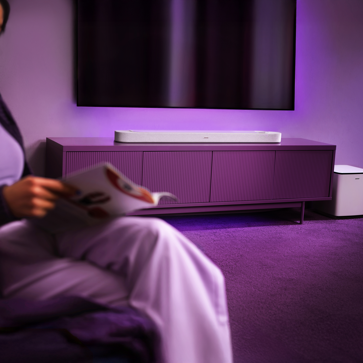 Eine Person liest ein Magazin vor einem lila Schrank mit einer Soundbar und einem Fernseher.