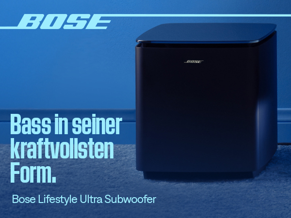 Ein schwarzer Bose Subwoofer steht auf einem blauen Teppich vor einer blauen Wand.