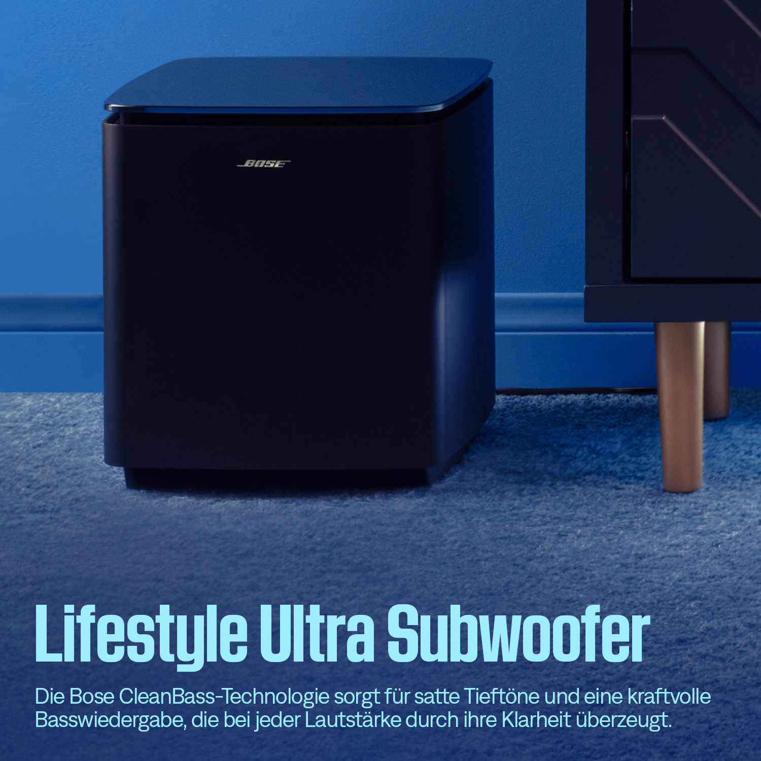 Dunkelblauer Bose Subwoofer steht auf einem blauen Teppich vor blauer Wand.