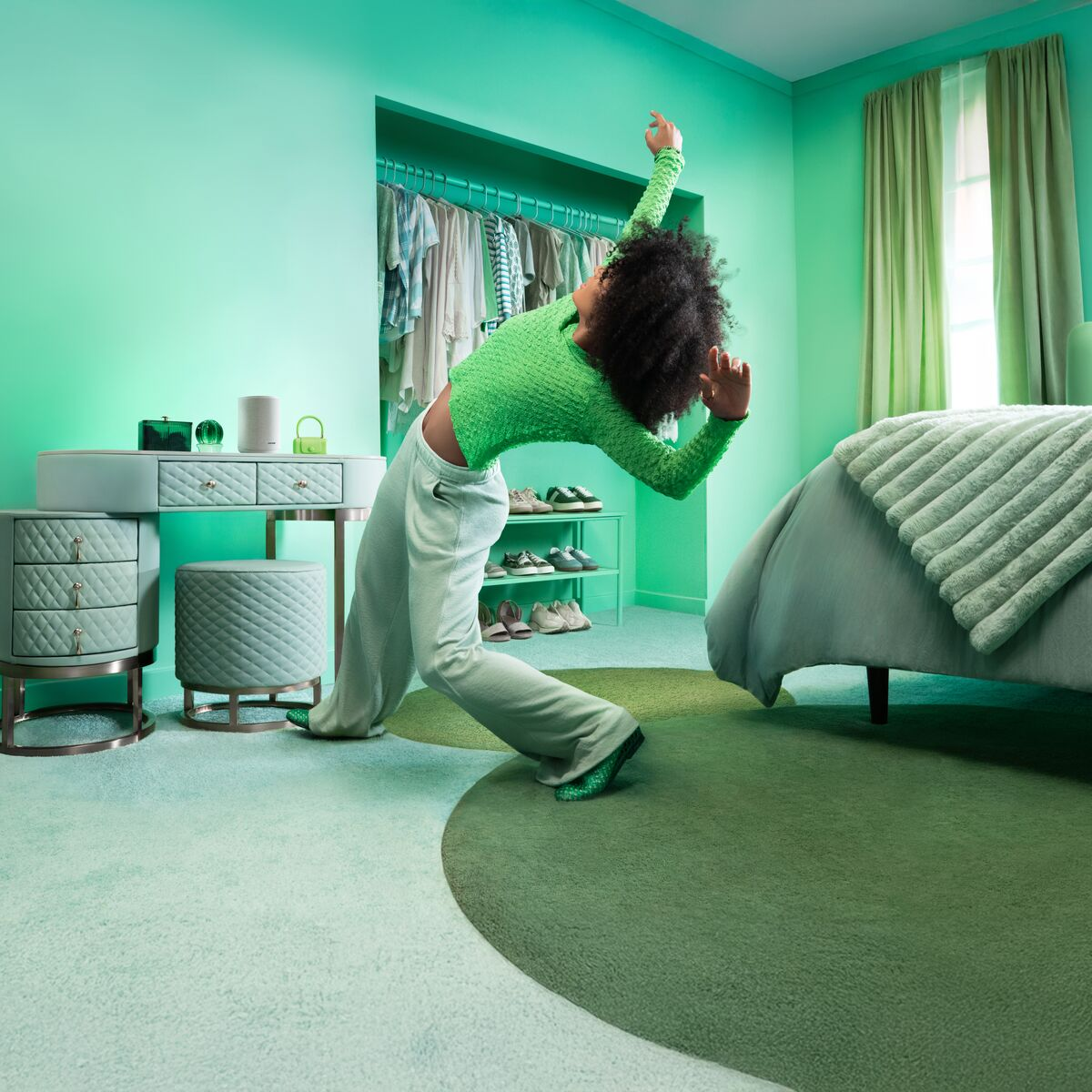 Eine Person in einem grünen Oberteil tanzt in einem mintgrünen Schlafzimmer mit Kleiderschrank, Schminktisch und Bett.