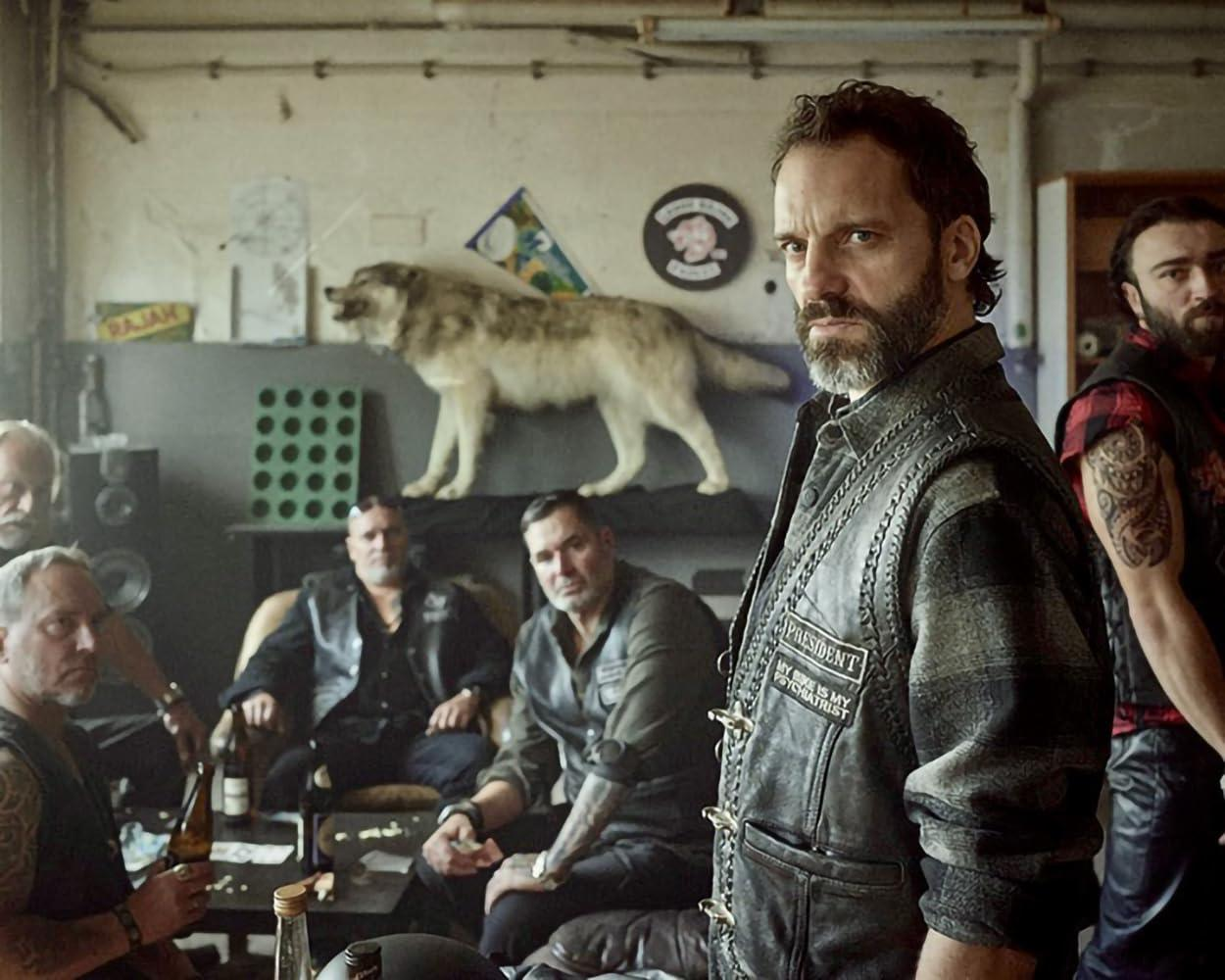 Eine Gruppe Männer in Lederkleidung sitzt in einem Raum mit einem Wolf auf dem Regal.