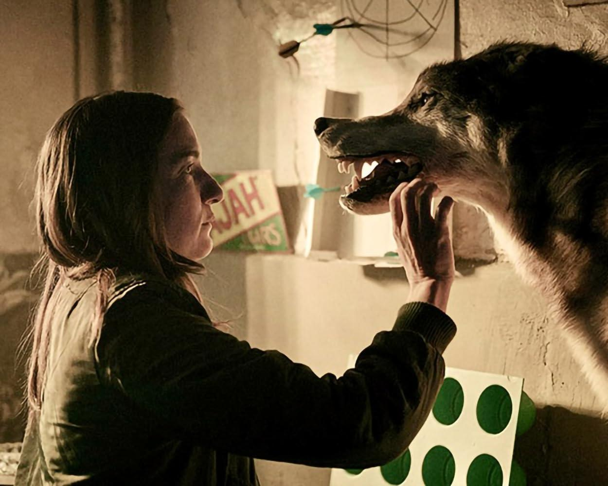 Eine Frau berührt das Maul eines ausgestopften Wolfs in einem schwach beleuchteten Raum.