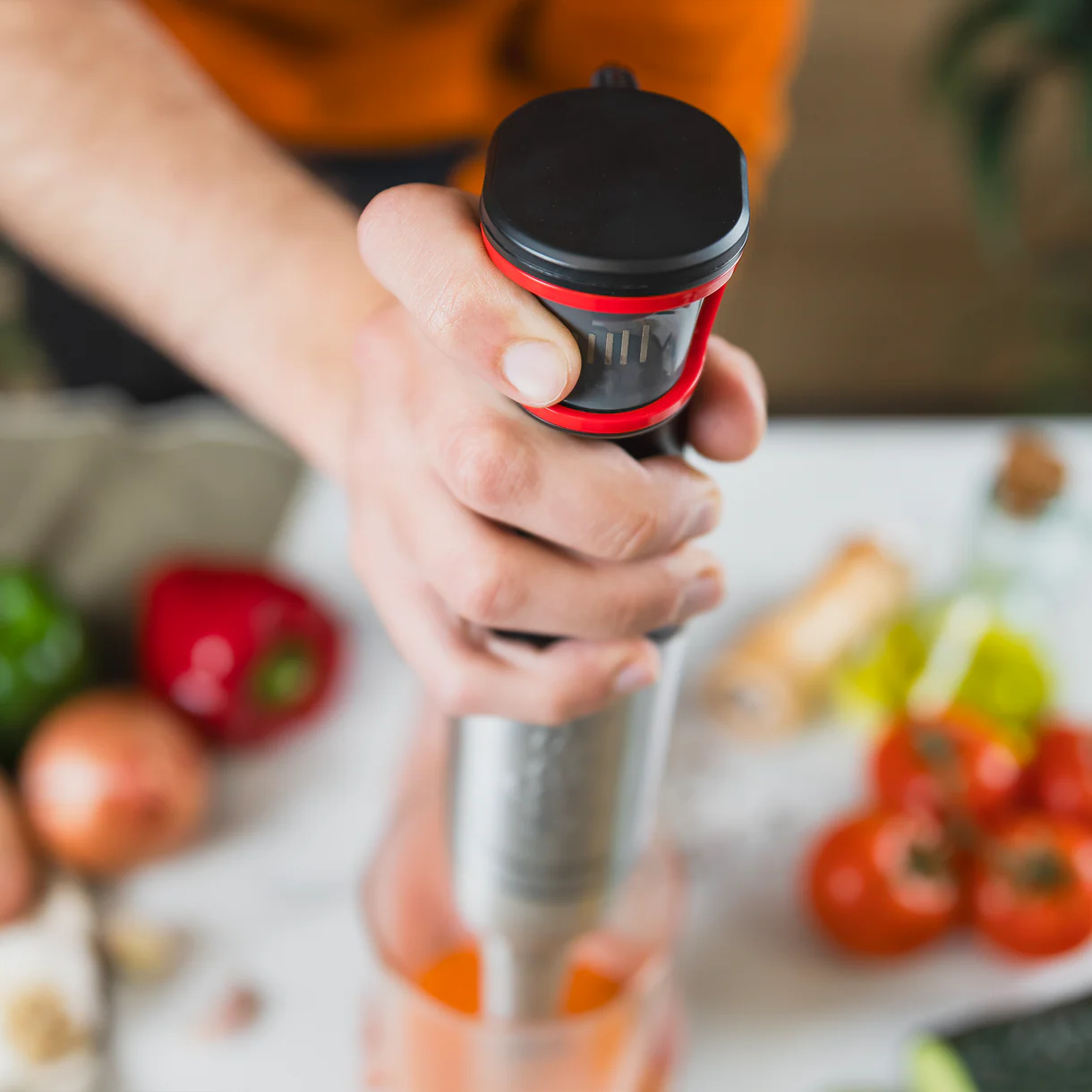 Una mano sostiene una batidora de inmersión sobre un vaso de líquido naranja.