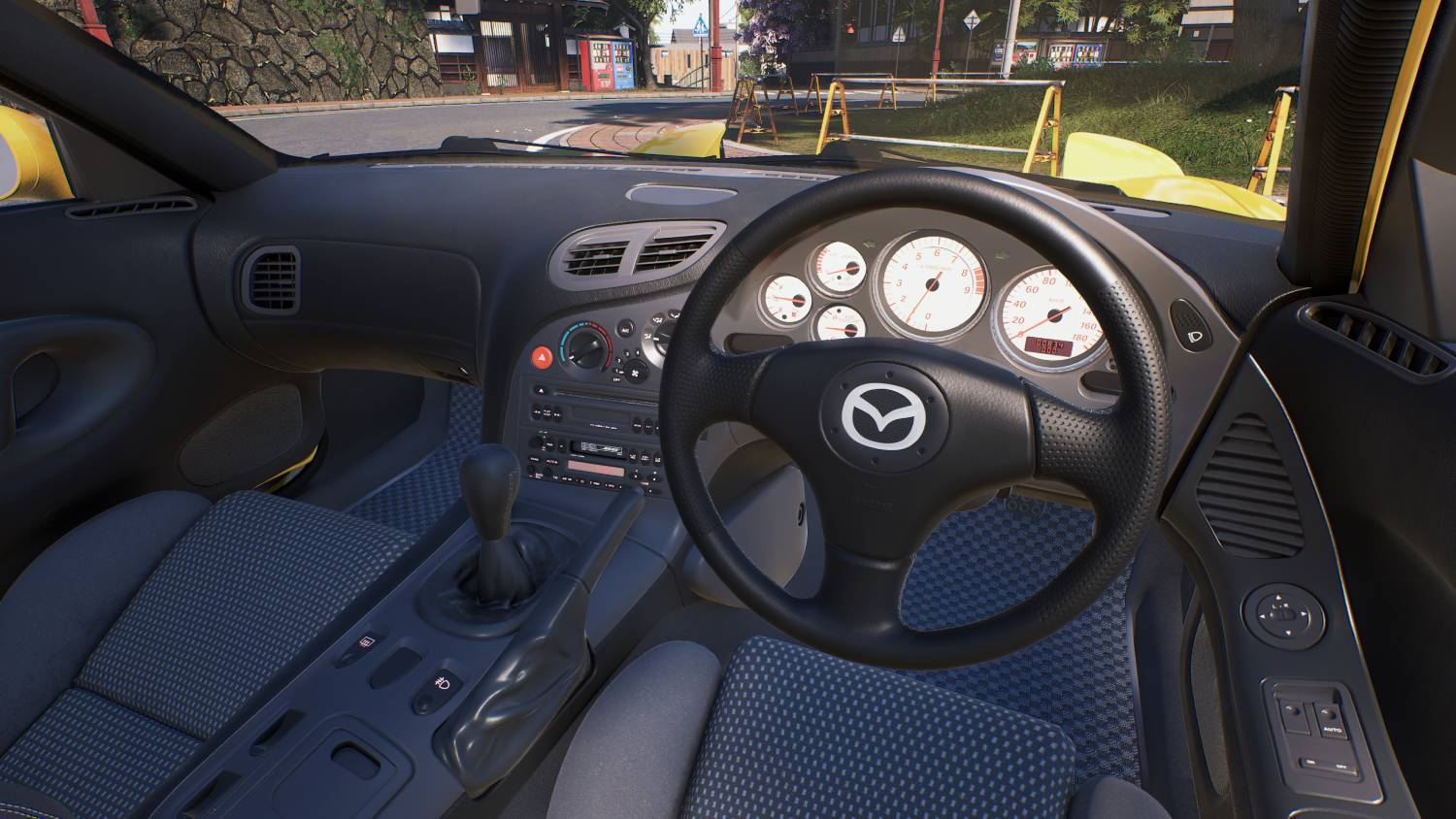 Vista interior de un Mazda RX-7 con volante negro, salpicadero y asientos de cuadros azules.