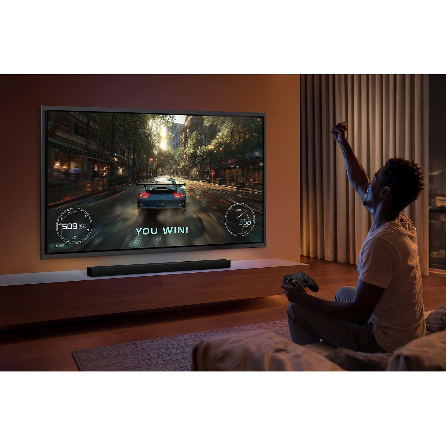 Man cheers in front of a TV screen displaying a racing game.