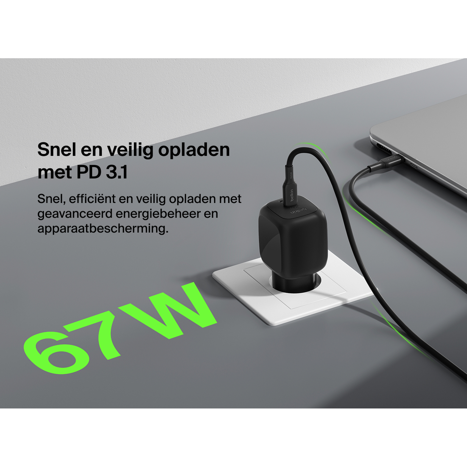 Black 67W charger plugged into wall, charging a laptop. Fast charging.