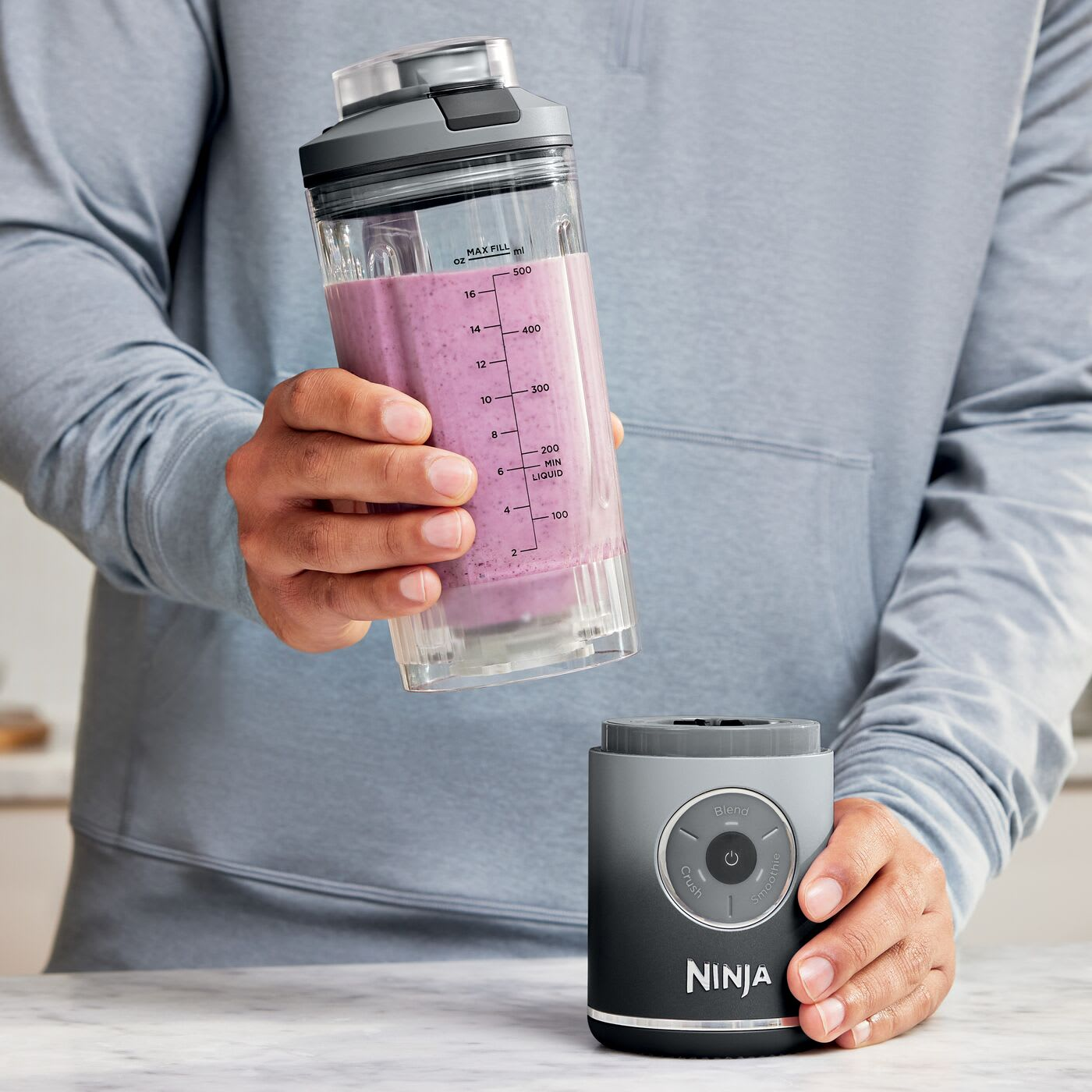 Eine Person hält einen Mixerbecher mit lila Smoothie über einen Ninja-Mixerfuß.