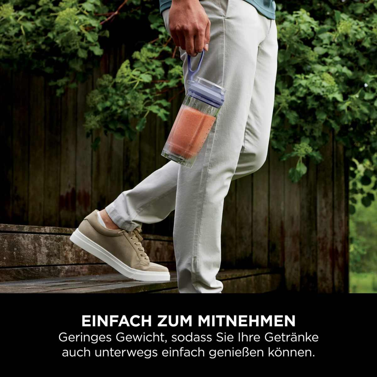 Une personne tient une tasse à smoothie, pantalon clair et chaussures, en extérieur.