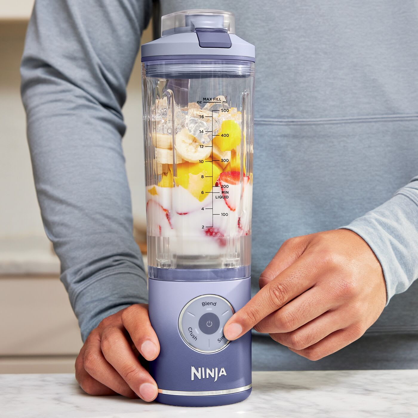 Personne appuyant sur le bouton d'un mixeur Ninja violet avec fruits et glace.