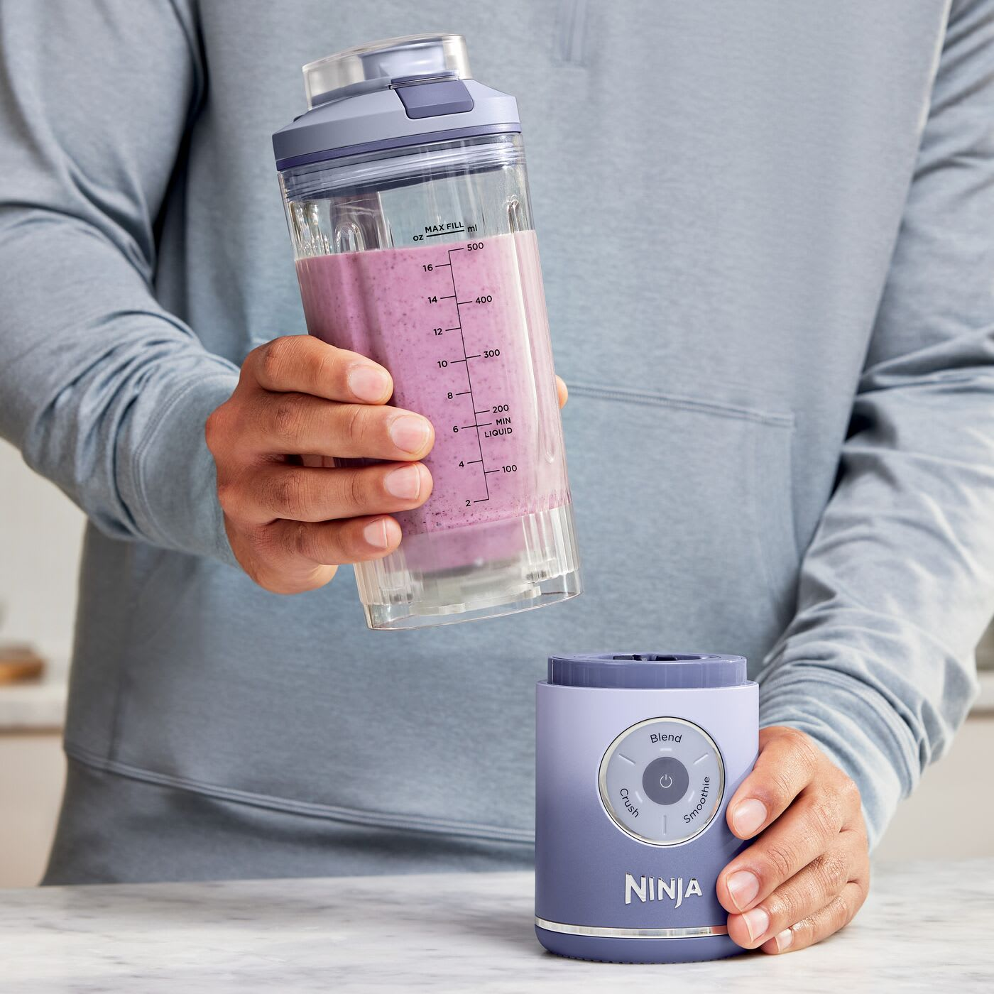 Une personne tient une tasse avec un smoothie violet au-dessus d'une base de mixeur Ninja violette.