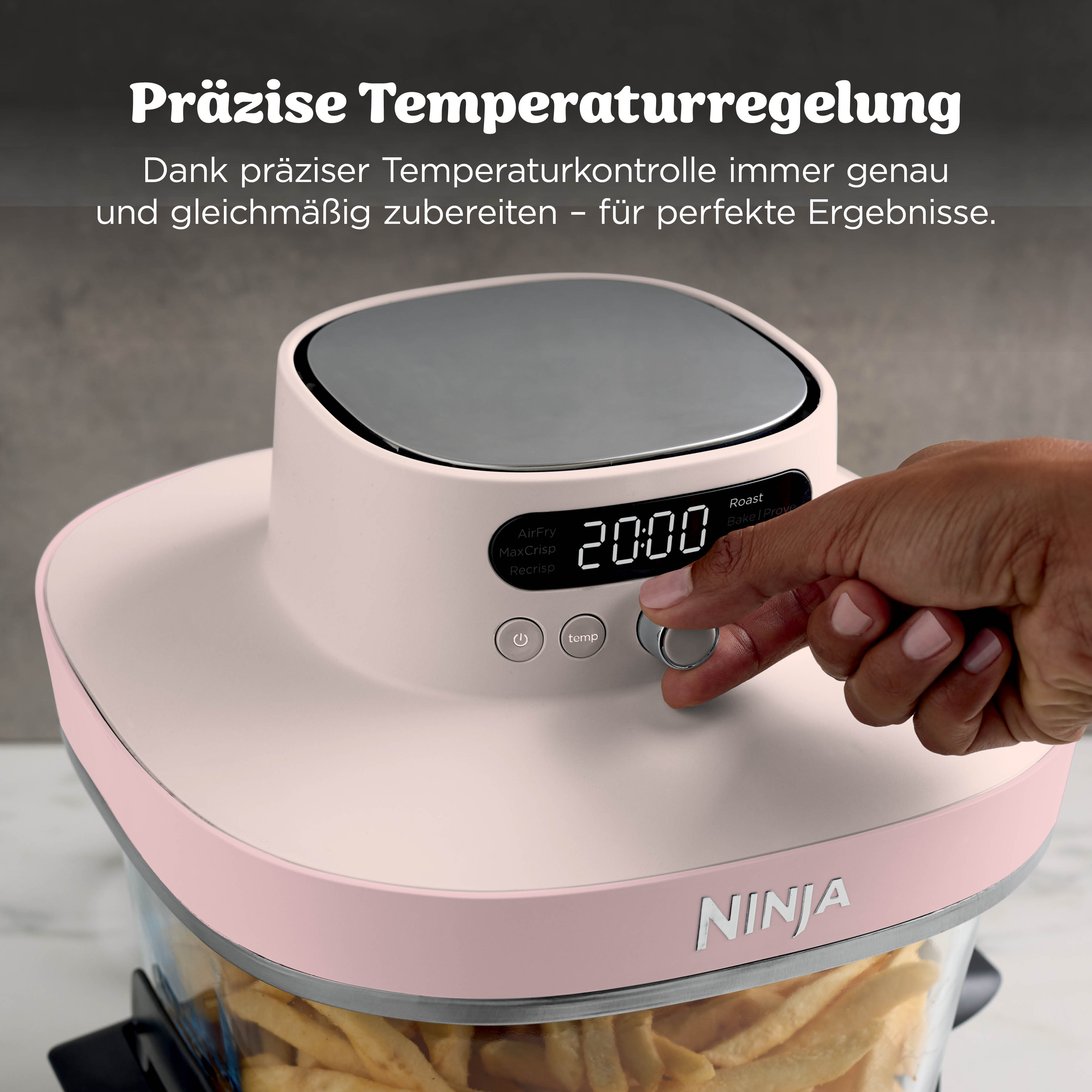 Eine Hand stellt einen rosa Ninja Heißluftfritteusen-Regler ein. Pommes sind im Korb.