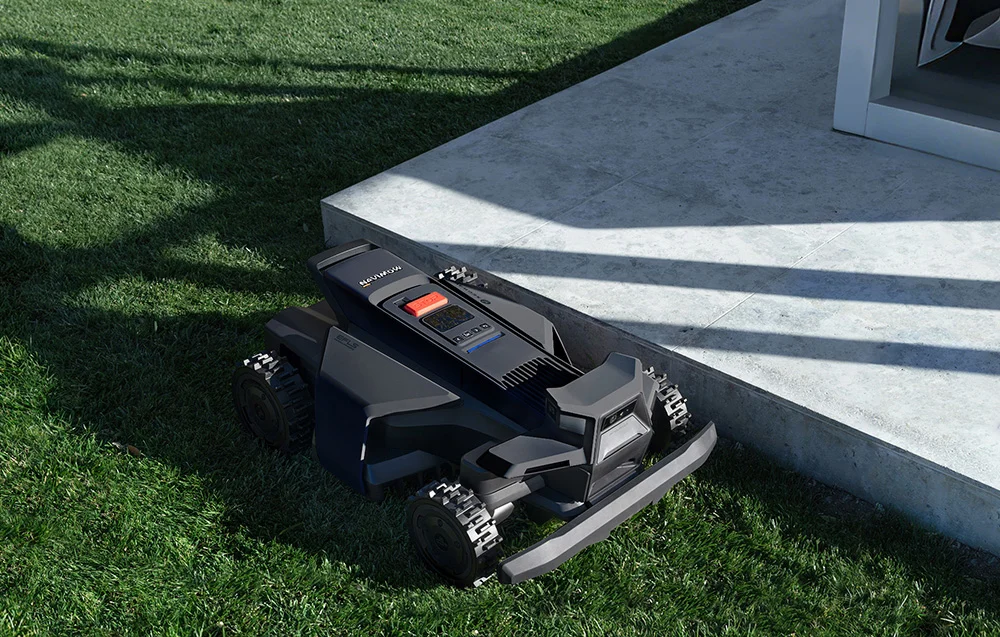 Egy fekete robotfűnyíró áll zöld füvön, betonfelület mellett.