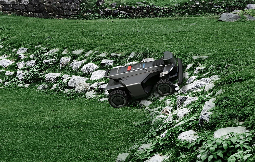 Egy sötétszürke robotfűnyíró egy sziklás, füves lejtőn navigál zöld növényzet mellett.