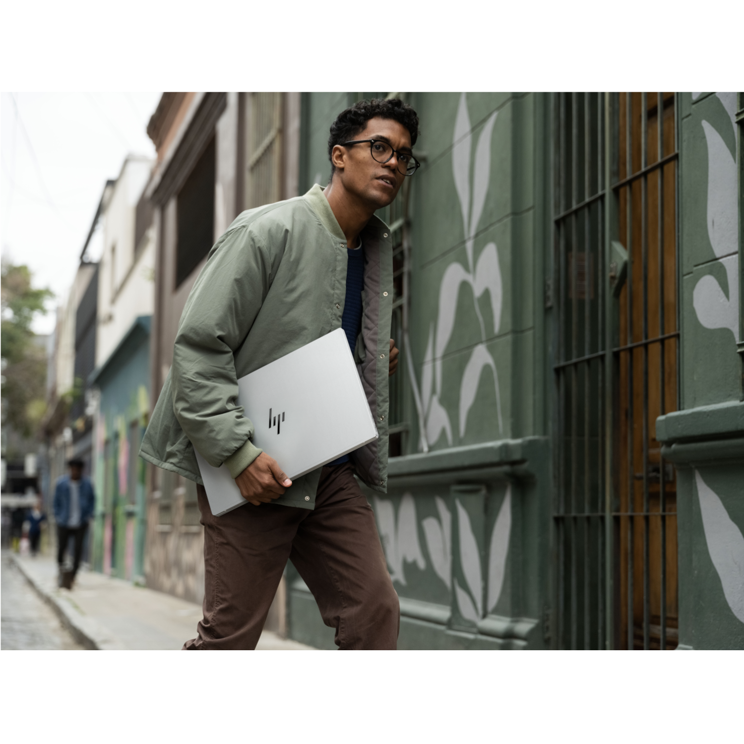 A man wearing glasses carries a laptop down a cobblestone street.