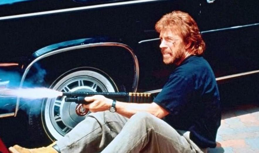 Ein Mann feuert eine Schrotflinte neben einem Auto ab.