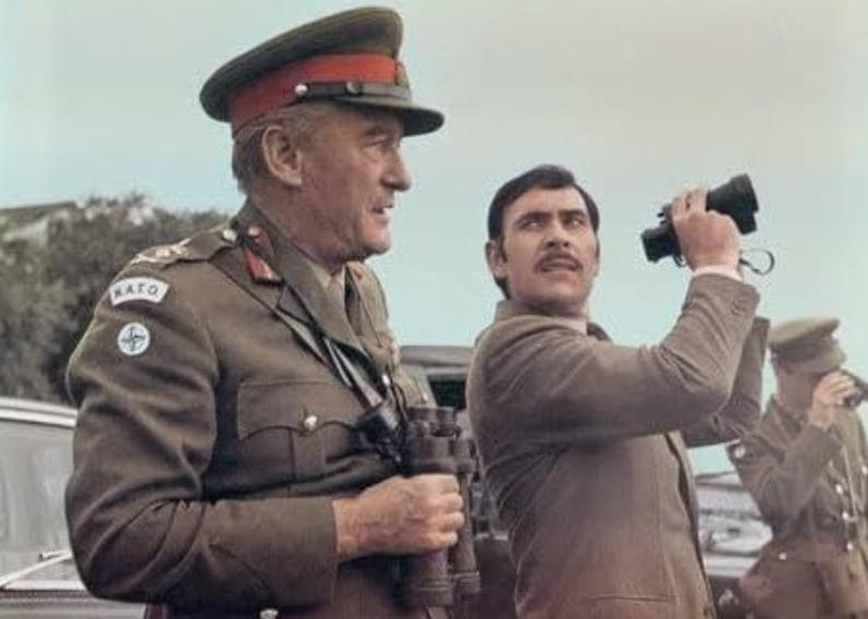 Ein General und ein Mann mit Fernglas stehen draußen.