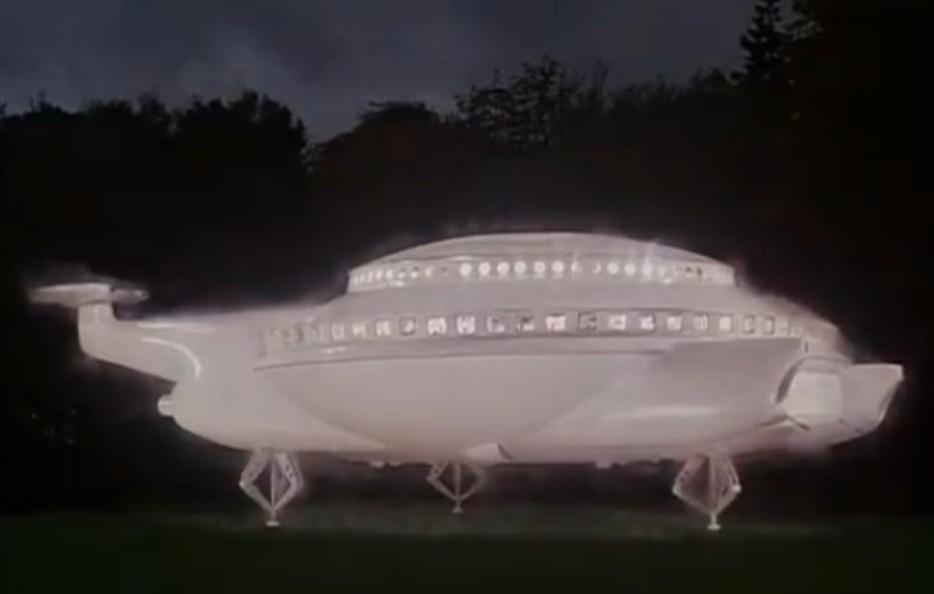 Ein weißes, leuchtendes UFO mit Fenstern steht auf Stelzen im Gras bei Nacht.