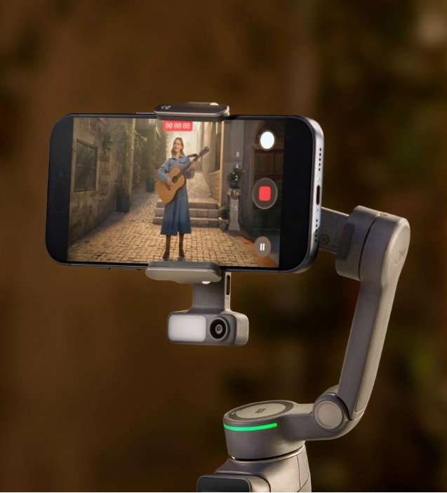 Smartfon nagrywa kobietę grającą na gitarze na brukowanej ulicy.