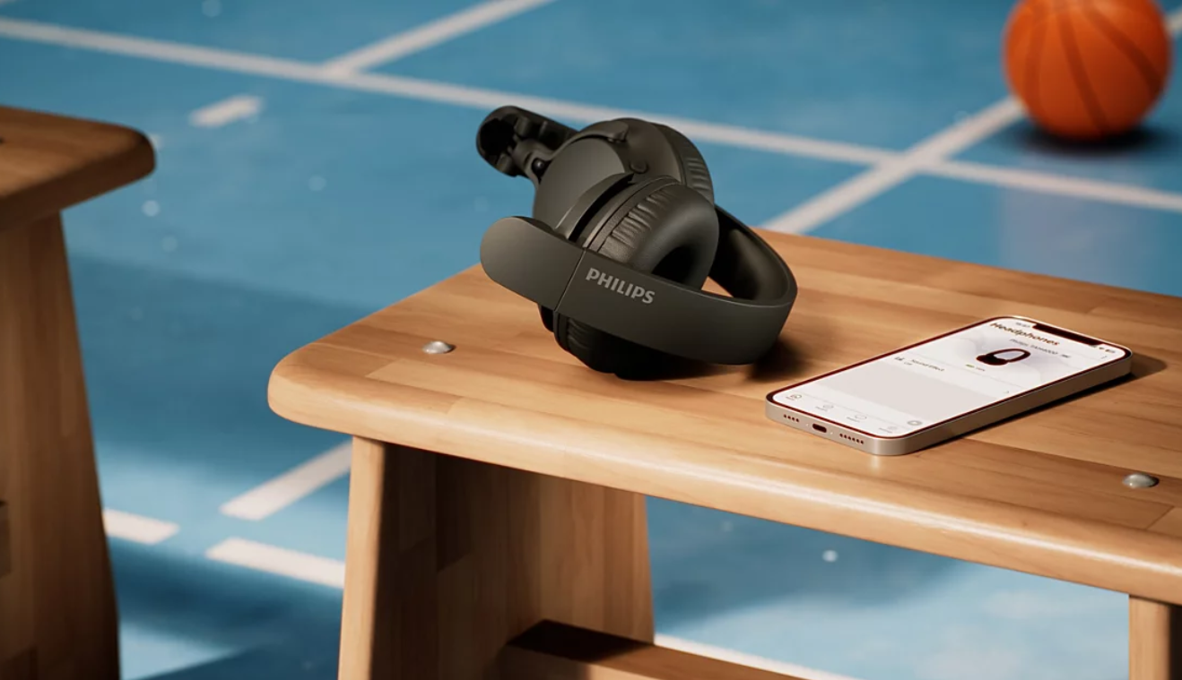 Czarne słuchawki i smartfon leżą na drewnianej ławce na niebieskiej sali sportowej.