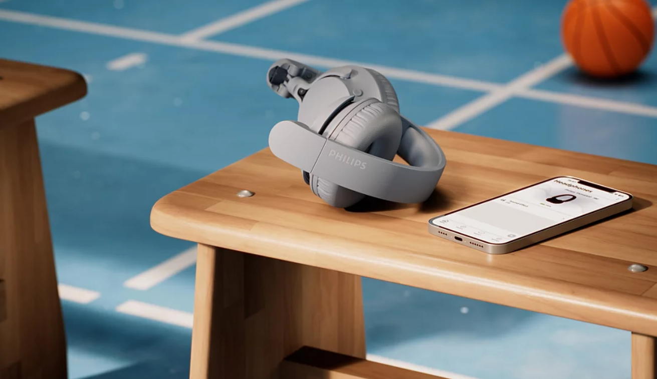 Szare słuchawki Philips i smartfon leżą na drewnianej ławce na niebieskiej podłodze sportowej.