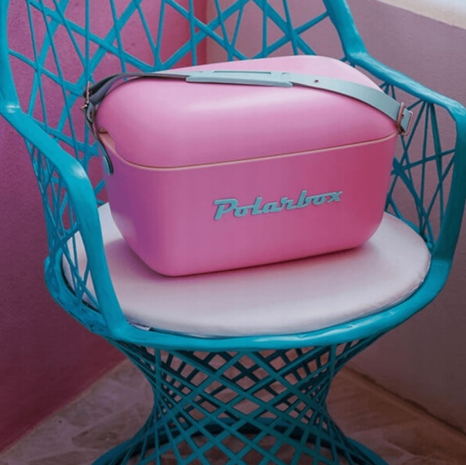 Różowa Polarbox z paskiem siedzi na turkusowym krześle z białym poduszką.
