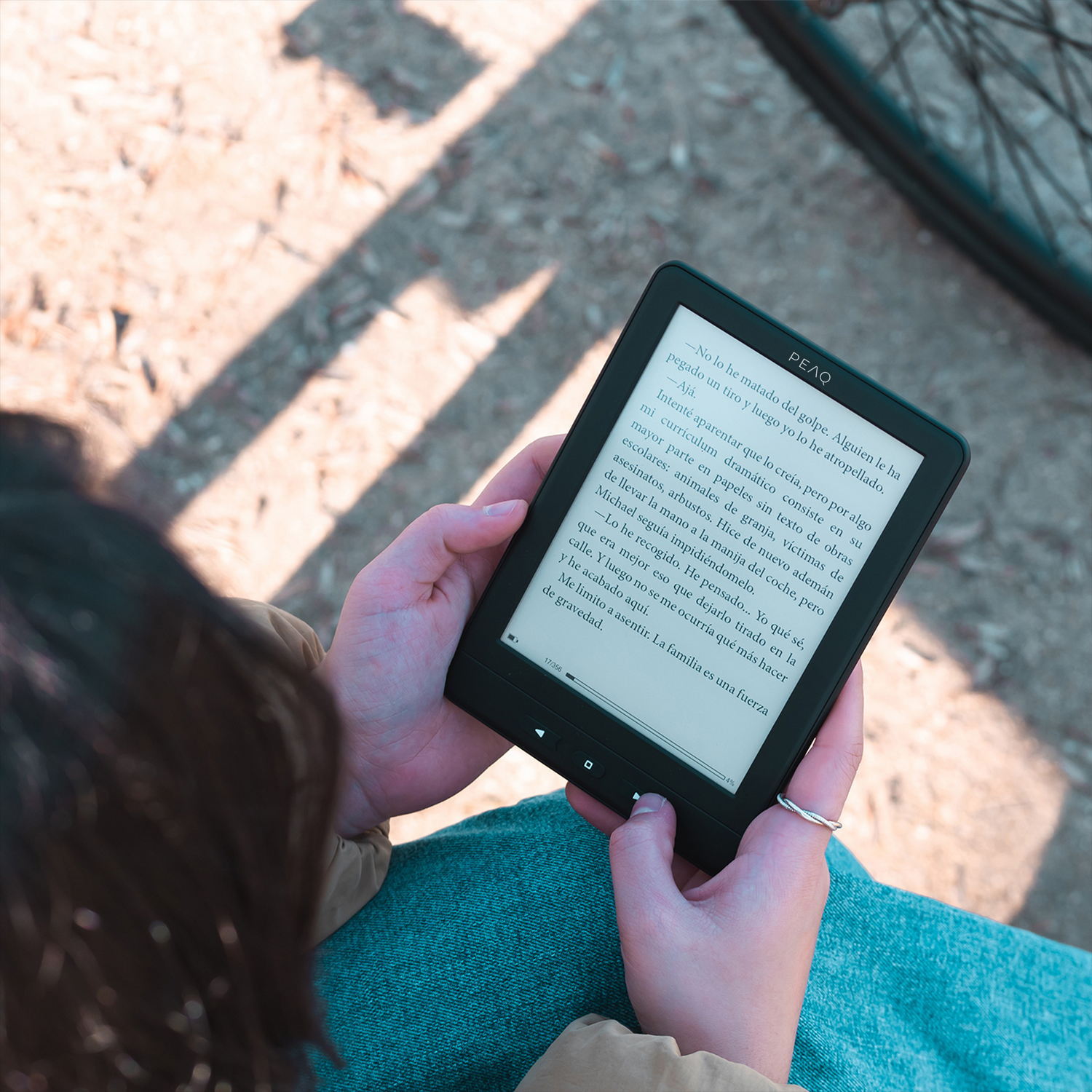 Manos sostienen un e-reader con un libro, brilla el sol.