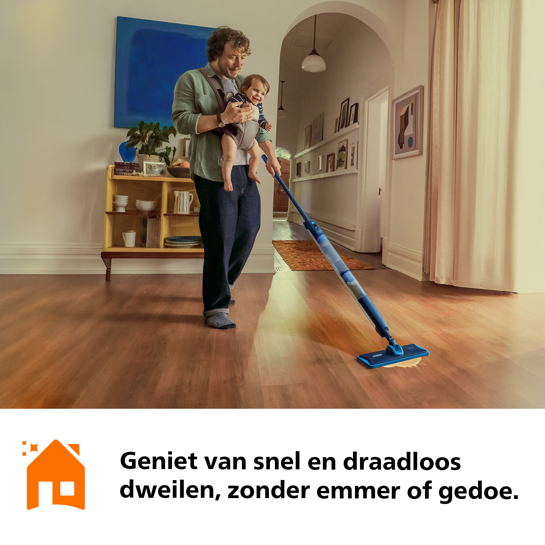 Man draagt baby en dweilt houten vloer met blauwe dweil.
