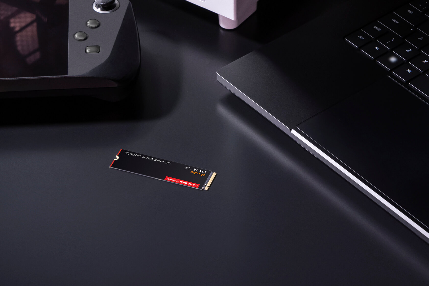 Ein NVMe SSD mit WD_BLACK SN7100 und Laptop auf dunklem Hintergrund.