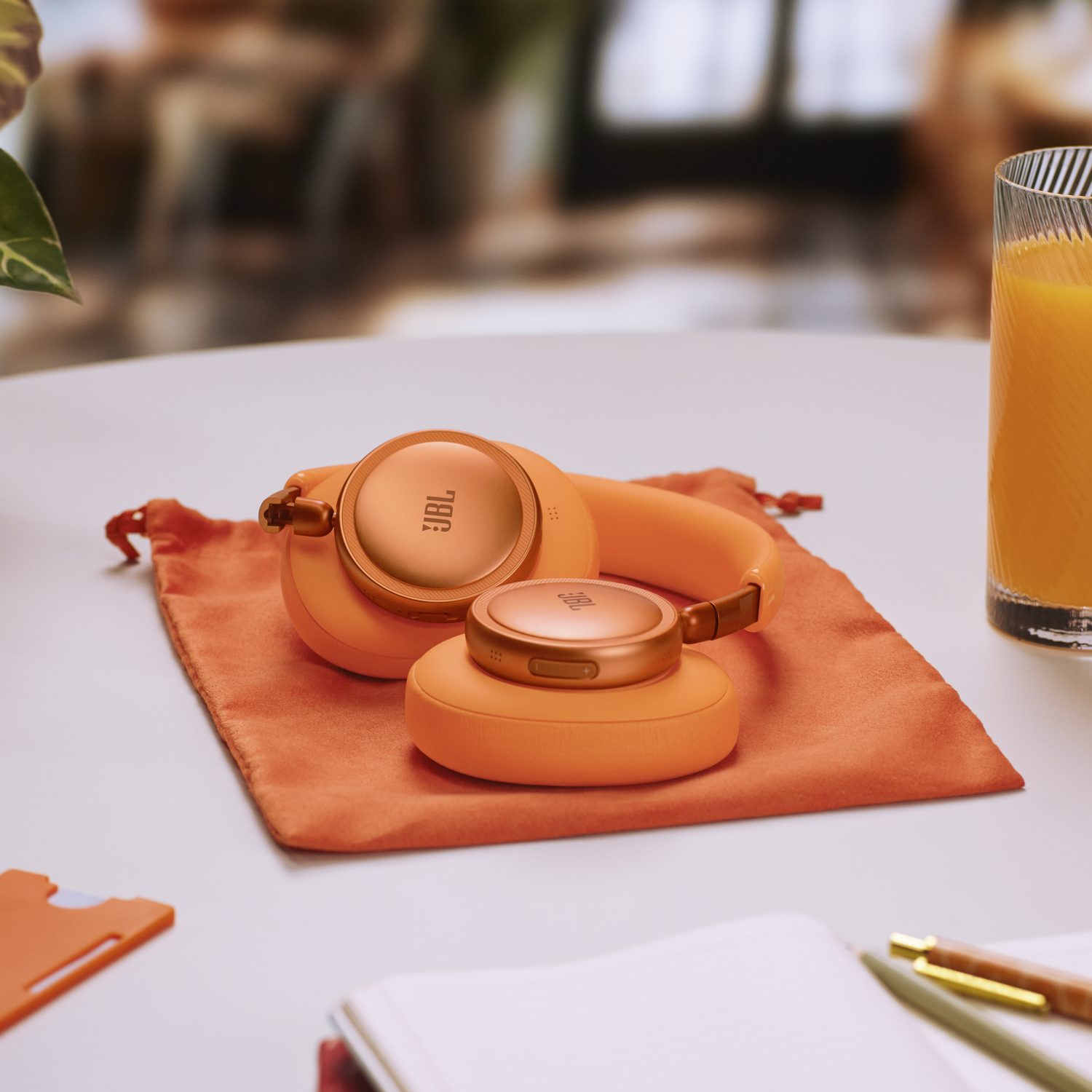 Orange JBL headphones rest on an orange cloth next to a glass of orange juice.