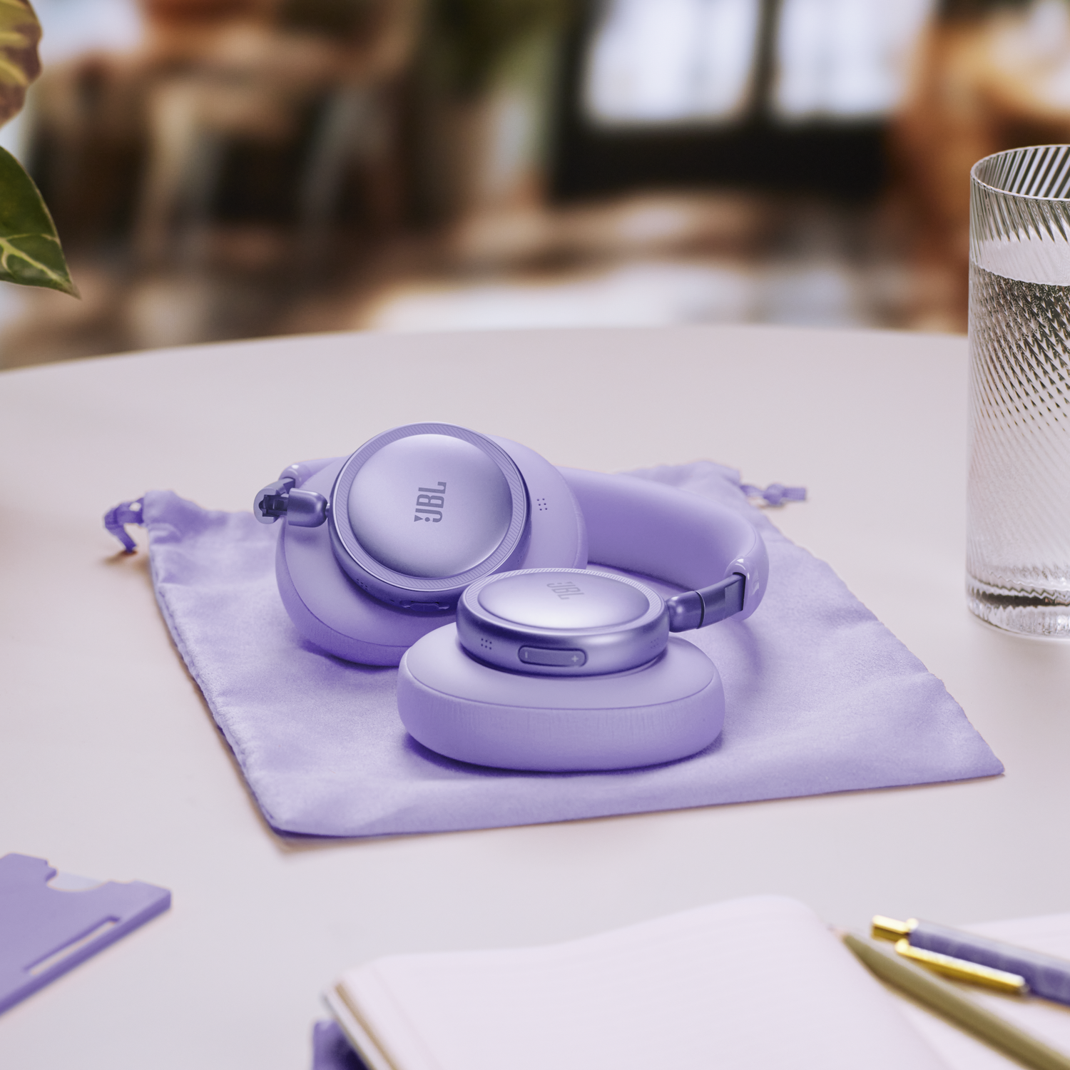 Purple JBL headphones rest on a cloth pouch, next to a glass.