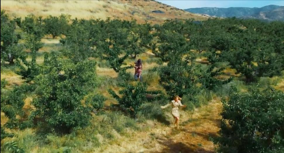 Zwei Frauen laufen durch einen Obstgarten mit vielen Bäumen und trockenem Gras.