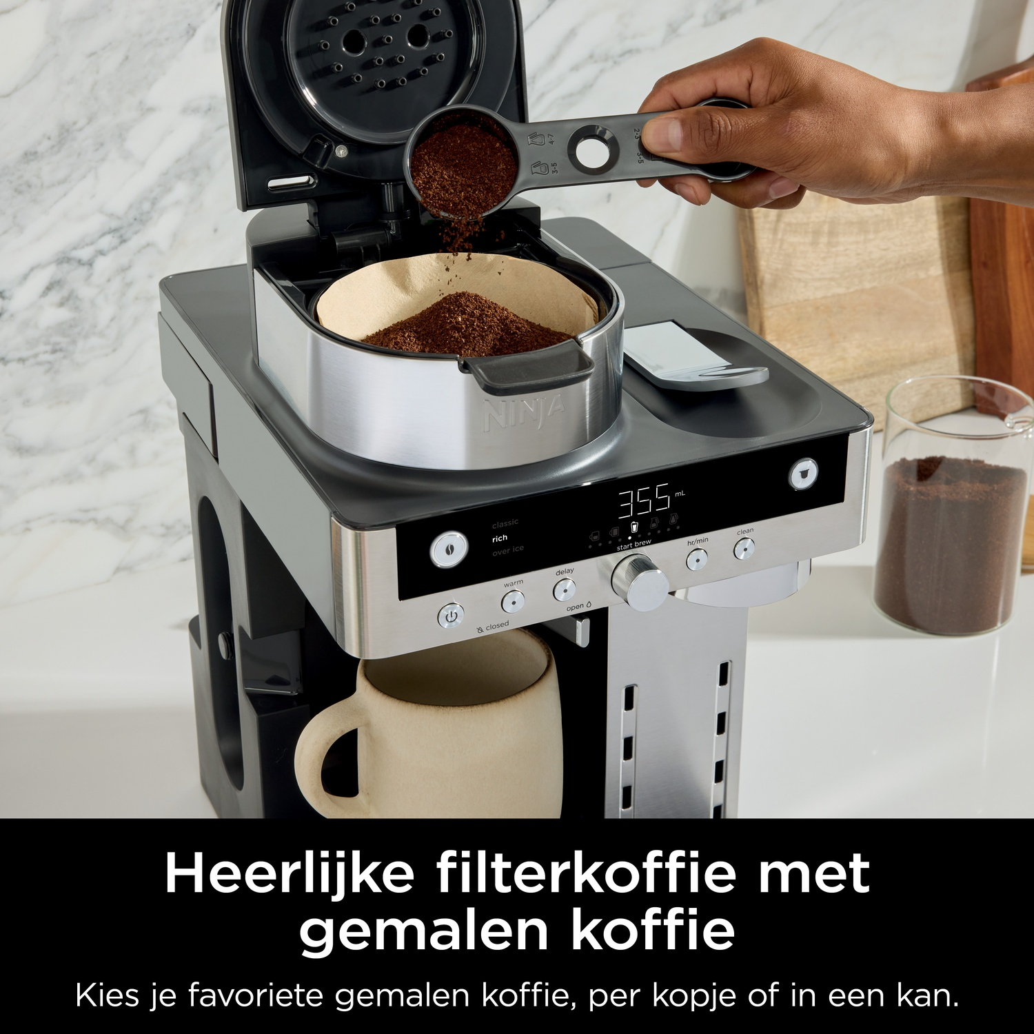 A hand adds coffee grounds to a filter in a coffee maker using a scoop.