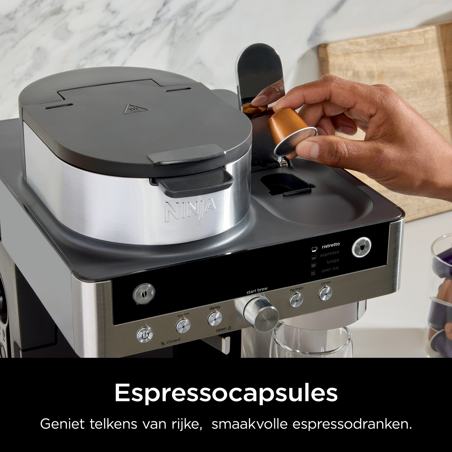 A hand inserts a brown capsule into a coffee machine with silver and black accents.