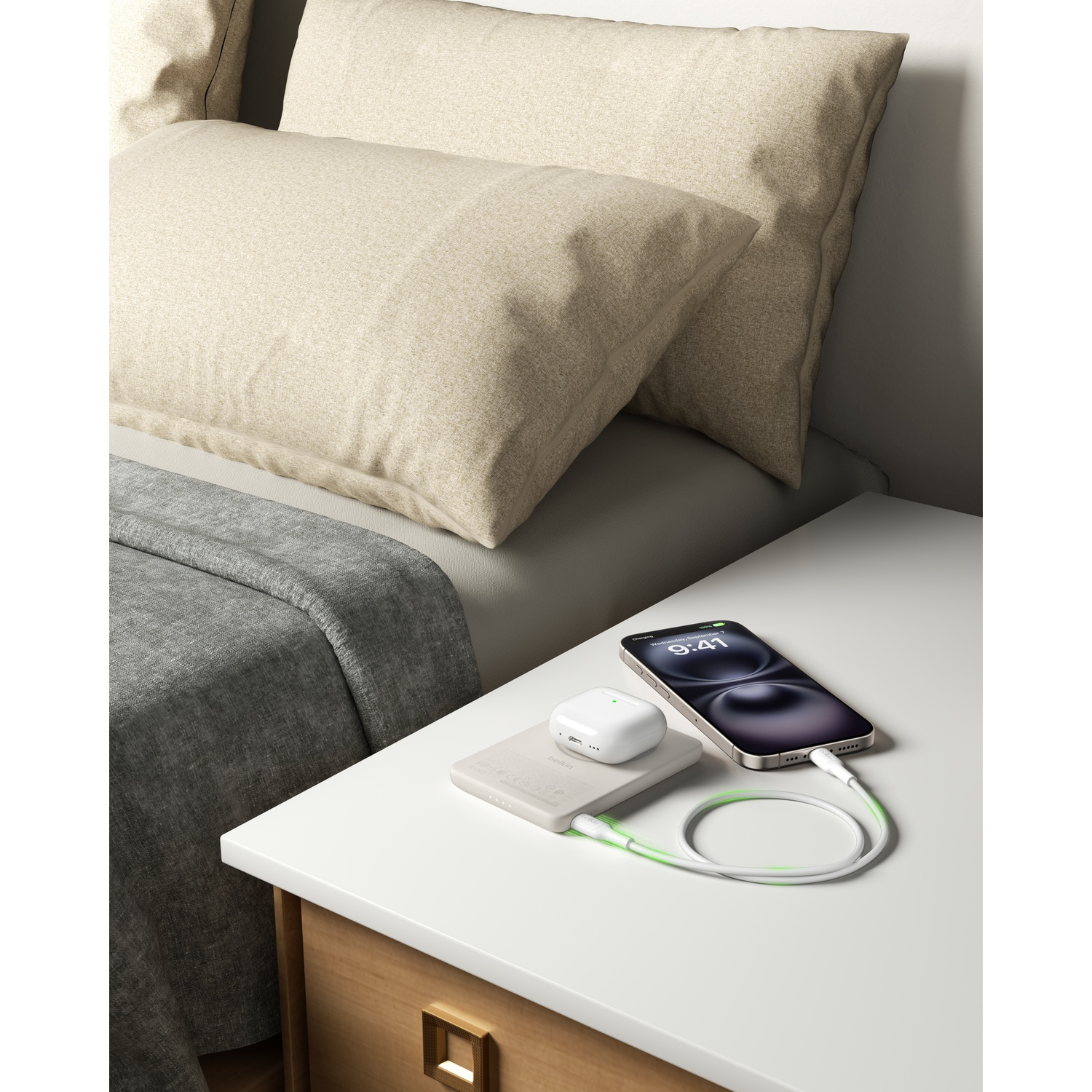 Une table de nuit avec téléphone, écouteurs et chargeur à côté d'un lit avec oreillers.