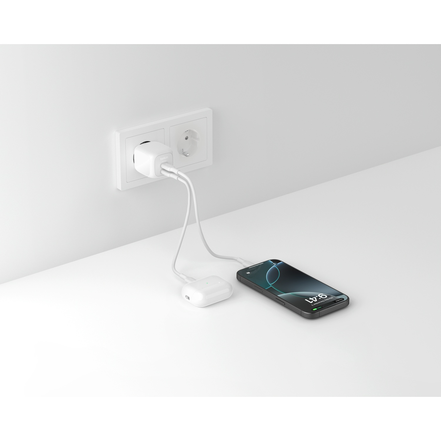 Un chargeur blanc est branché à une prise murale, chargeant un smartphone et des écouteurs.