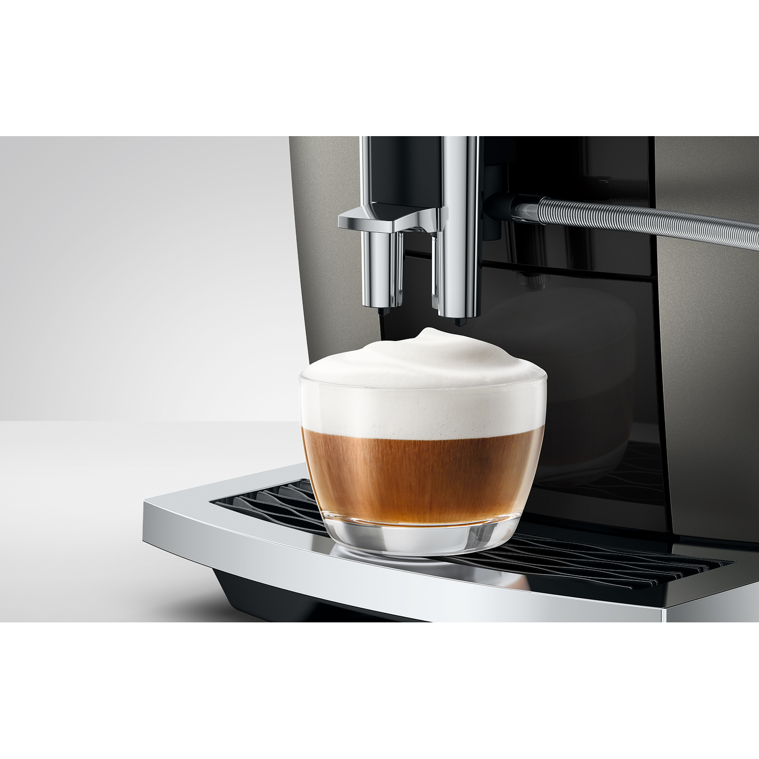Een glas koffie met schuim staat op een chromen lekbak van een koffiezetapparaat.