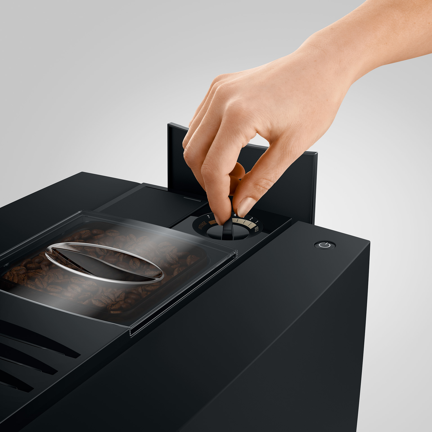Een hand draait aan een knop op een koffiezetapparaat met koffiebonen.