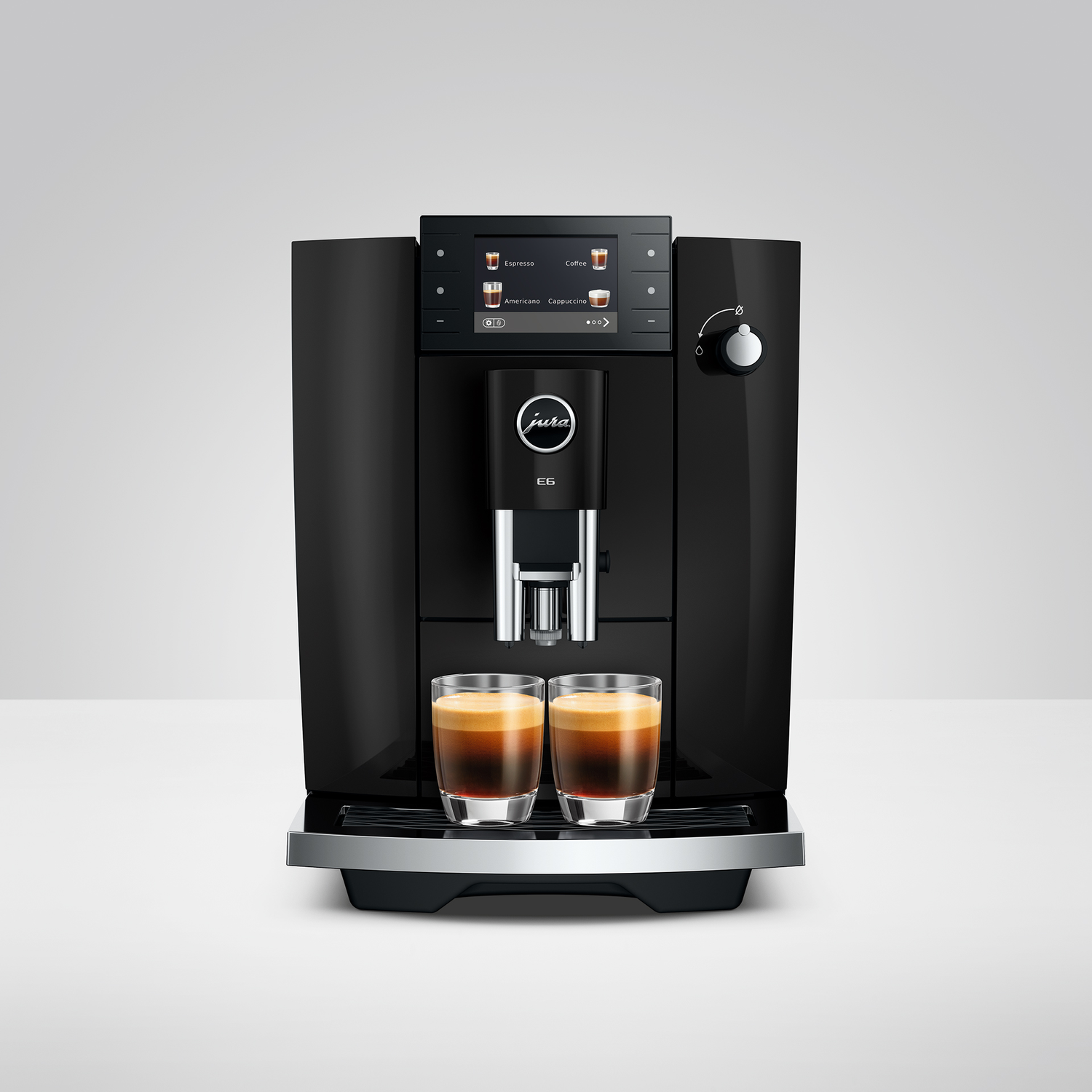 Zwarte koffiemachine met twee glazen espresso op de voorgrond.