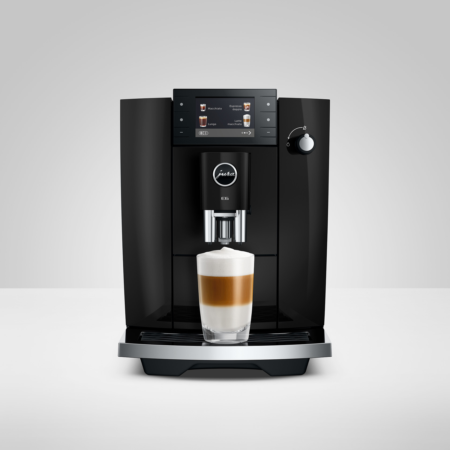 Zwarte Jura E6 koffiemachine schenkt een gelaagde latte in een glas.